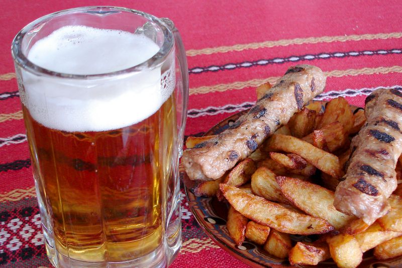 Bierkrug mit hellem, schäumendem bulgarischem Bier, danaben Teller mit Imbiss
