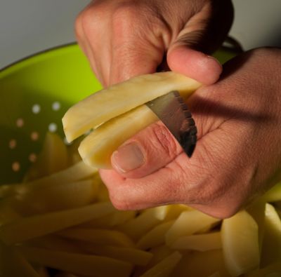Hand mit Messer schneidet Streifen aus Kartoffel für belgische Pommes Frittes