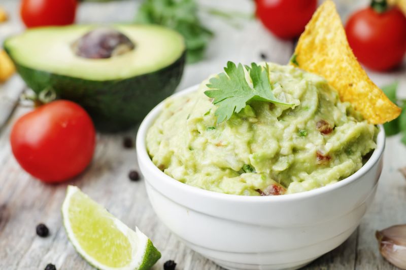 Schalte frischer Guacamole auf Tisch mit Avocado, Limettenstück und Tomaten