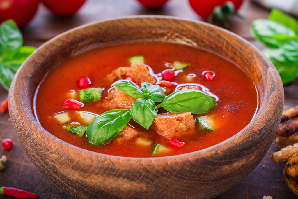 Gazpacho in Holzschale, garniert mit Gurken- und Tomatenstückchen, Basilium-Blättchen und Croutons