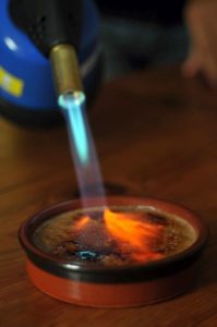 Flamierbrenner wirft Flamme auf Crèmes Brulées, um den Zucker zu karamellisieren.