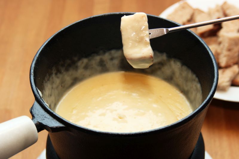 Topf mit Käsefondue, eine Gabel mit einem Stück eingetunktem Brot darüber.