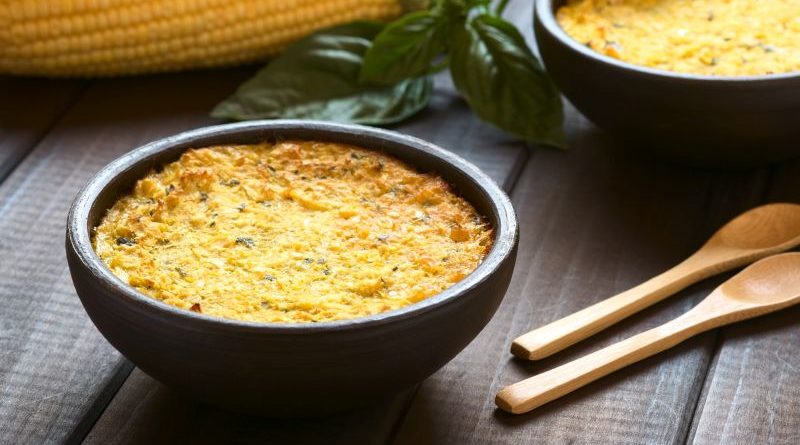 Dunkler Holztisch mit einer Schale Pastel de Choclo, im Hintergrund ist ein Maiskolben zu sehen.