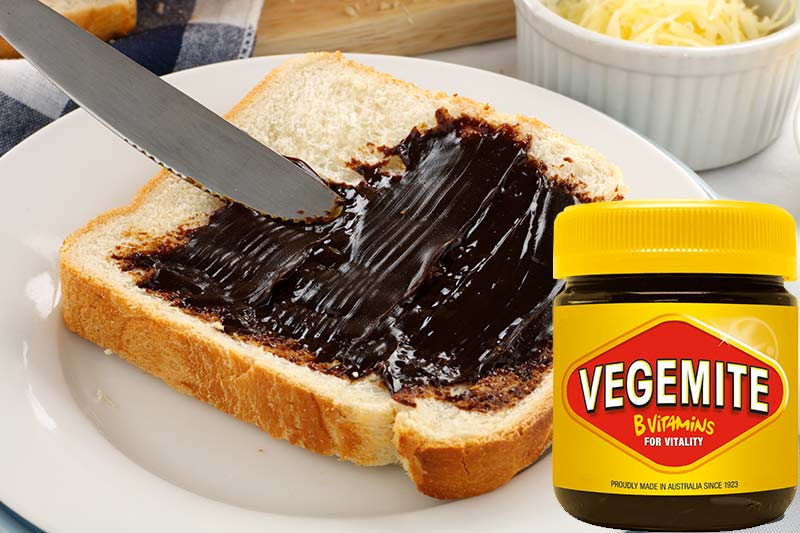Scheibe Toast wie bestrichen mit Vegemite, rechts ein Glas Vegemite